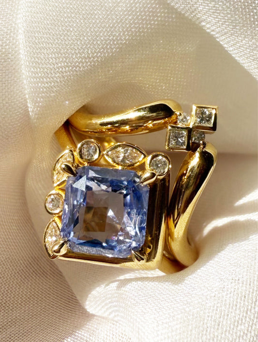 Gold ring with a blue gemstone and smaller diamonds on a white fabric background
