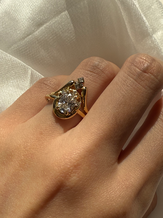 Gold ring with a large diamond on a hand against a white fabric background