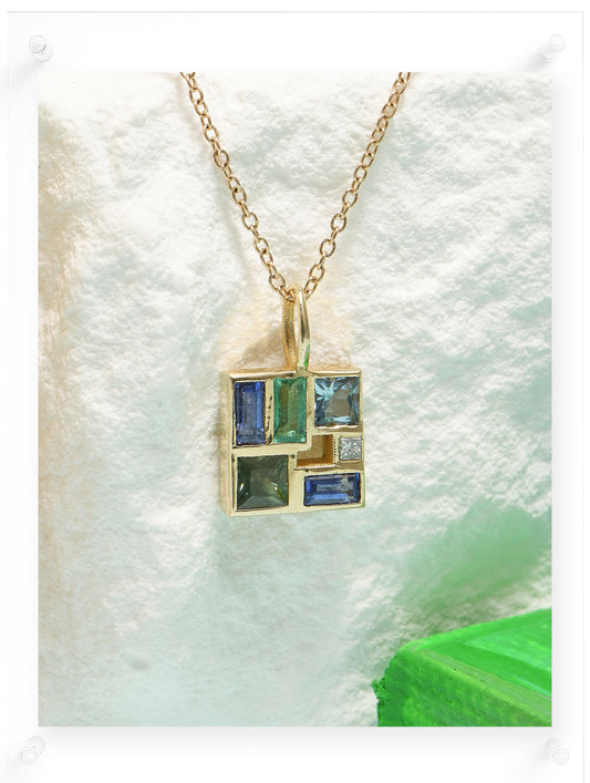 Gold necklace with a pendant featuring green and blue gemstones on a white background