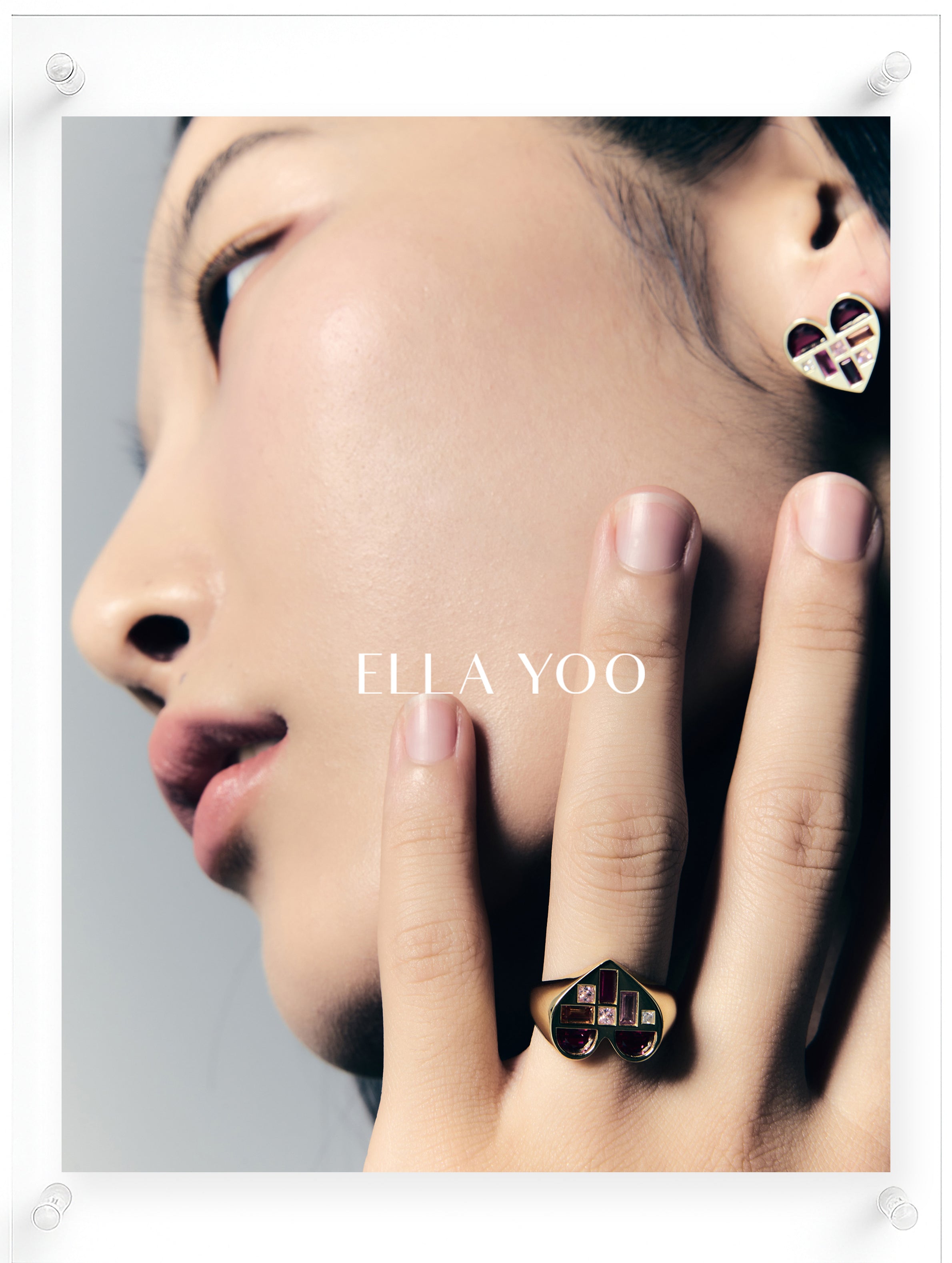 Model wearing a 14K yellow gold heart shaped ring and matching stud earrings with pink sapphire and multicolor gemstone accents by Ella Yoo J