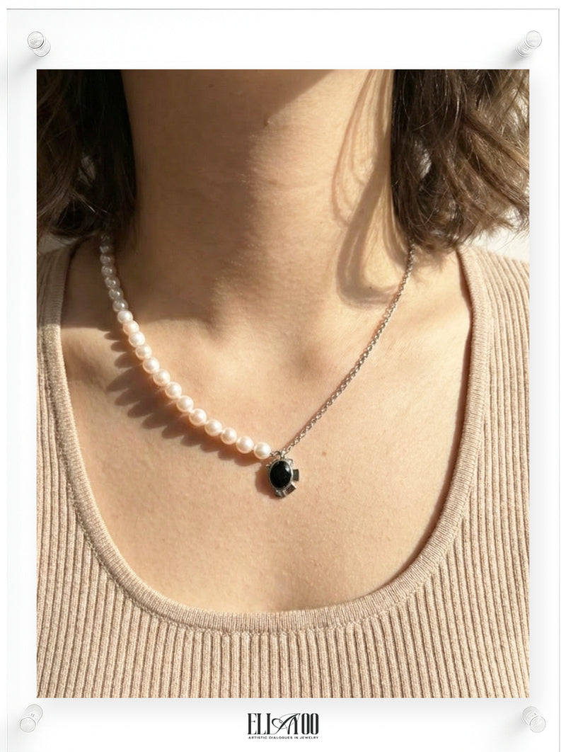 Pearl necklace with a black pendant worn by a person in a beige top.