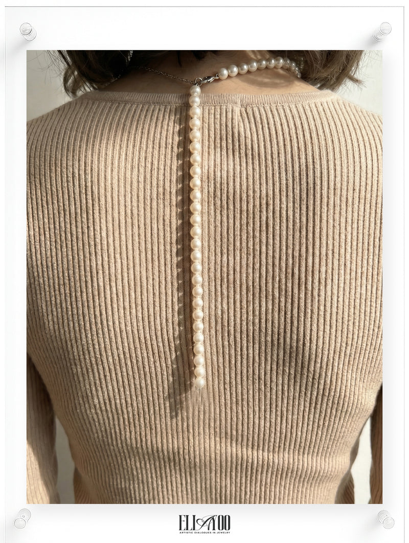 Person wearing a beige ribbed sweater with a pearl necklace draped over the shoulder.