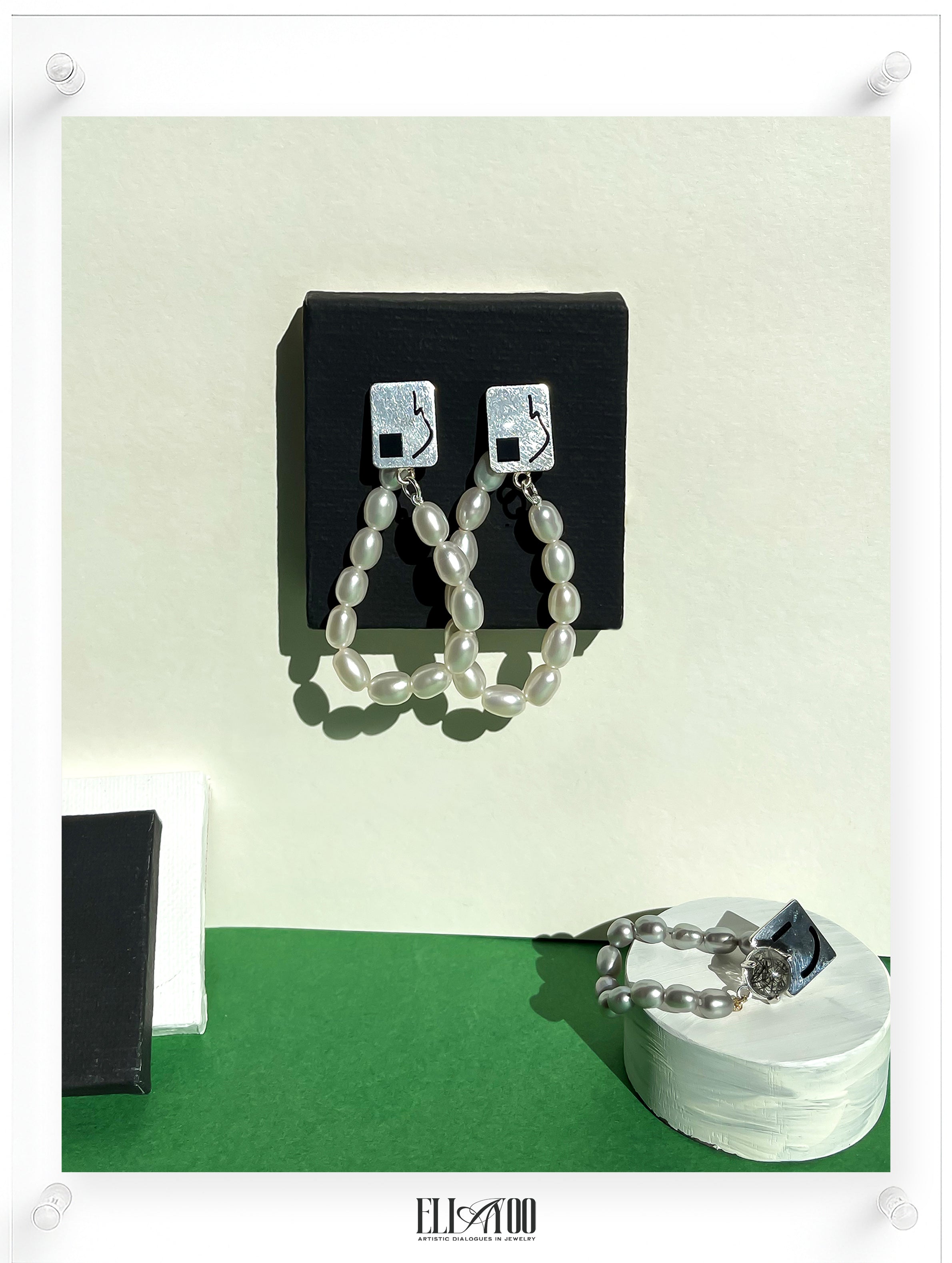 Contemporary pearl drop earrings displayed in a modern gallery-style setting, featuring organic freshwater pearls and geometric silver studs