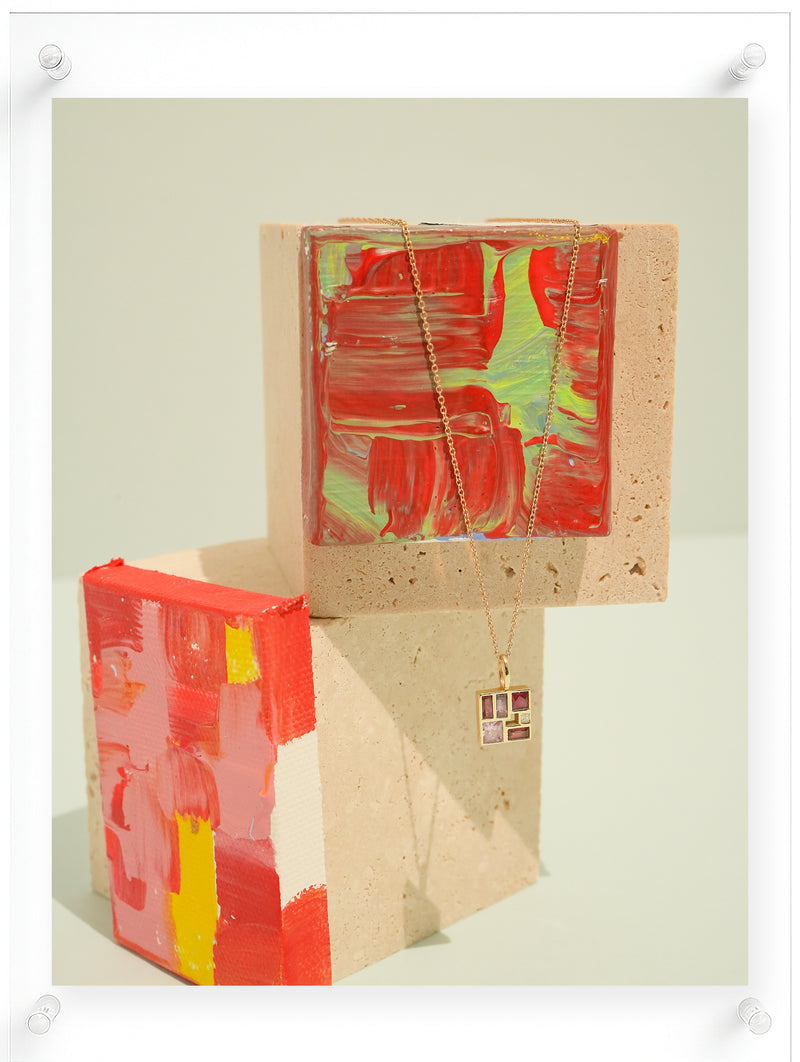 14K yellow gold geometric gemstone pendant necklace with pink tourmaline and diamond, displayed on hand-painted abstract art blocks, contemporary fine jewelry by Ella Yoo