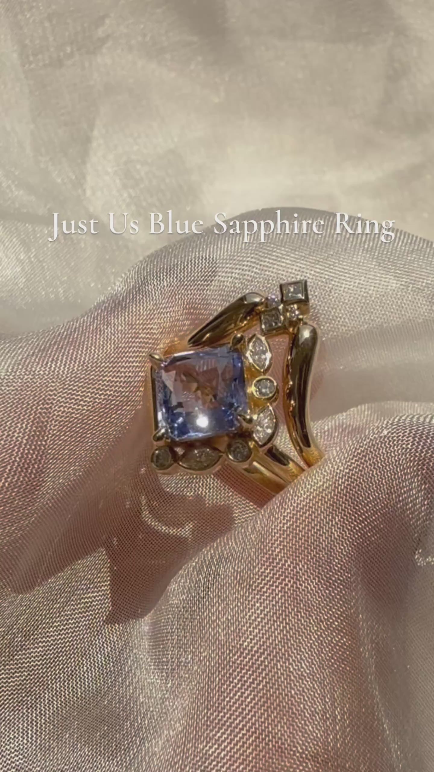 video showing Gold ring with a blue gemstone and smaller diamonds on a white fabric background