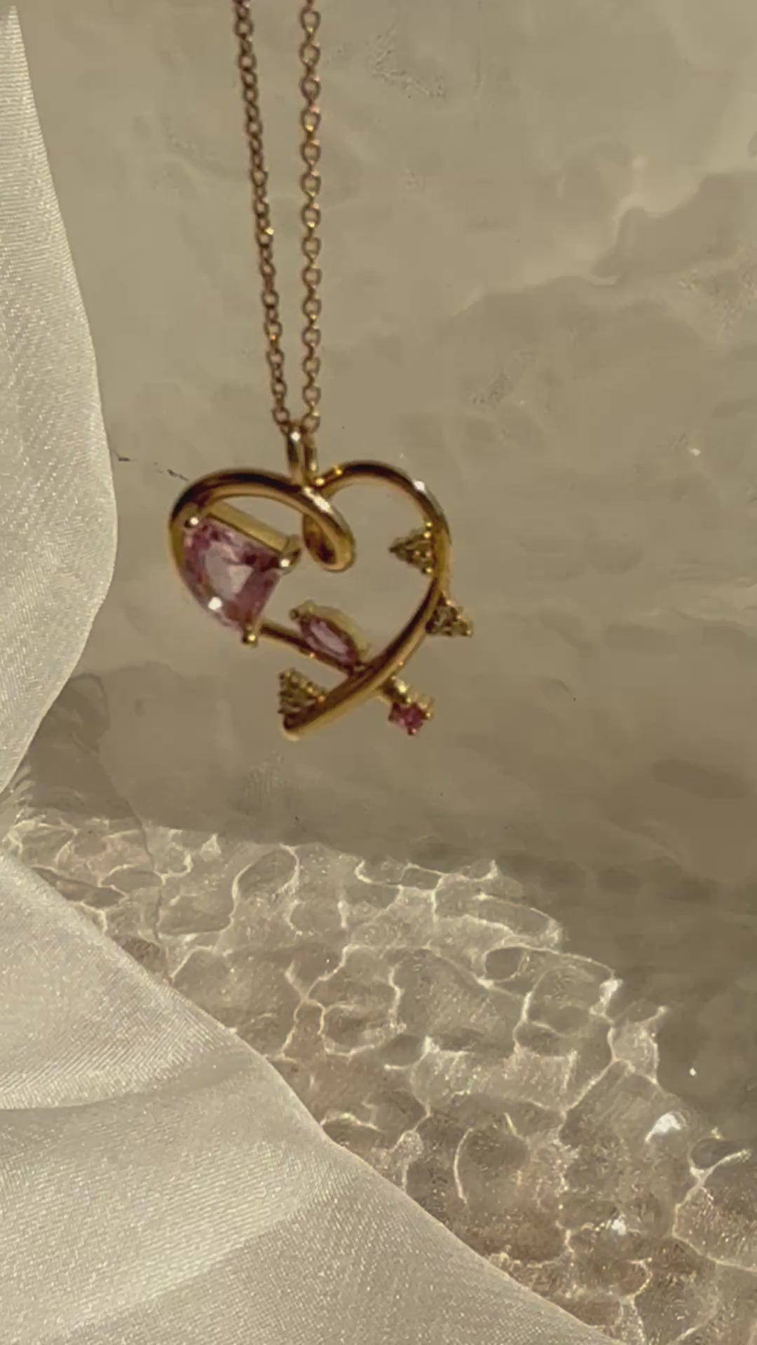 Rotating view of a 14K yellow gold open heart necklace featuring an asymmetrical pink sapphire and geometric sapphire accents, inspired by Bauhaus design philosophy.